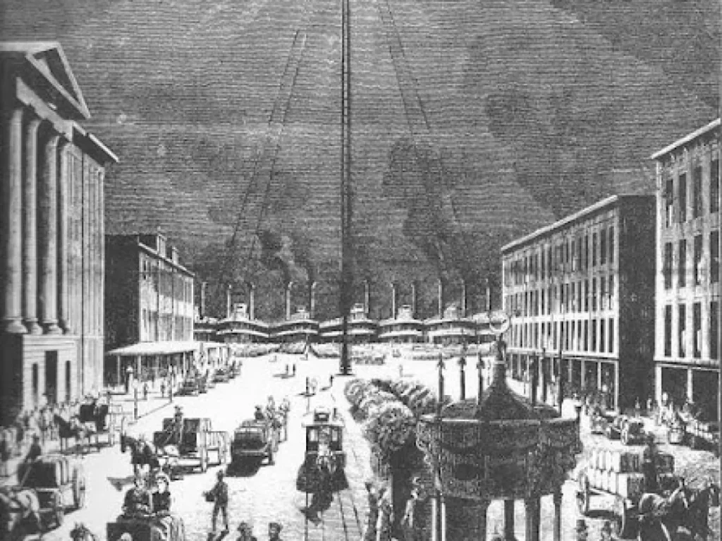 A black-and-white vintage illustration of a busy city street with horse-drawn carriages, people walking, historic buildings, and a tall pole or structure rising in the center. Factories with smokestacks are visible in the background.