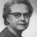 Black and white portrait of an older woman with short, curly hair, wearing glasses, a dark suit jacket, a light blouse, and a pearl necklace. She is looking slightly to the side with a neutral expression.